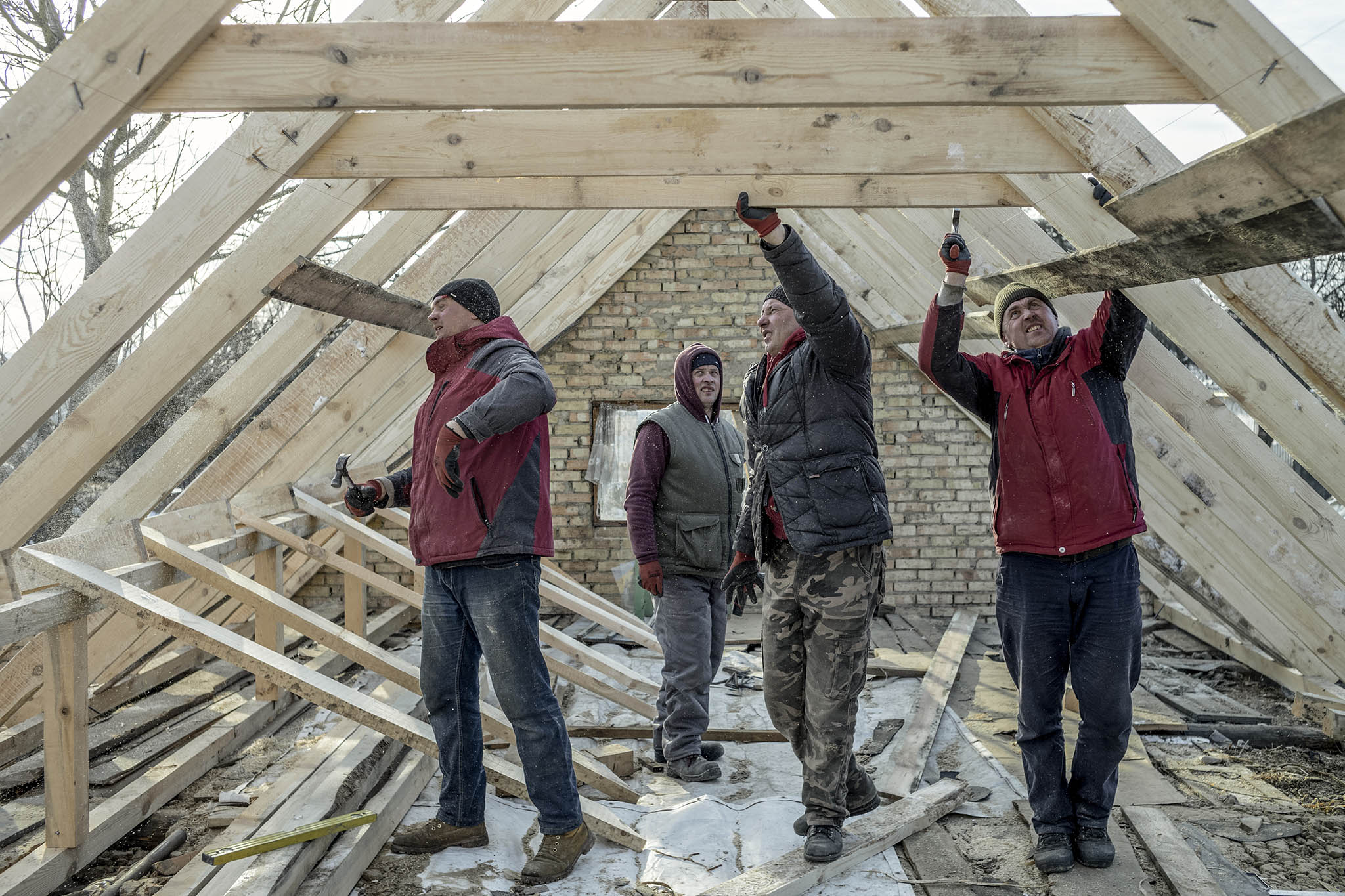 Workers rebuild the roof of a house in the Kyiv suburb of Bucha. February 9, 2023. (Emile Ducke/The New York Times)