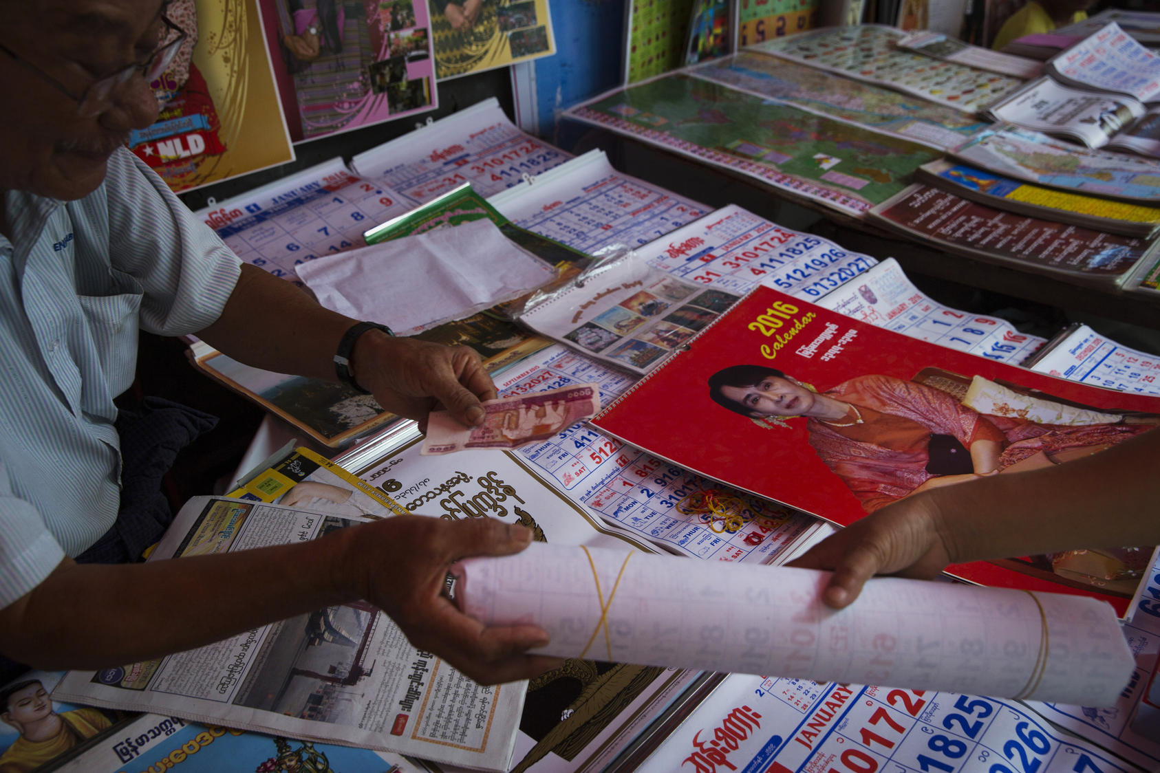 A woman purchases a calendar of Aung San Suu Kyi – who says she plans to circumvent the ban on her becoming president that the generals wrote into the Constitution – in Yangon, Myanmar, Nov. 10, 2015. Vestiges of Myanmar’s police state, alive and well, will wield enormous influence even with the lopsided election triumph by Aung San Suu Kyi’s Party.