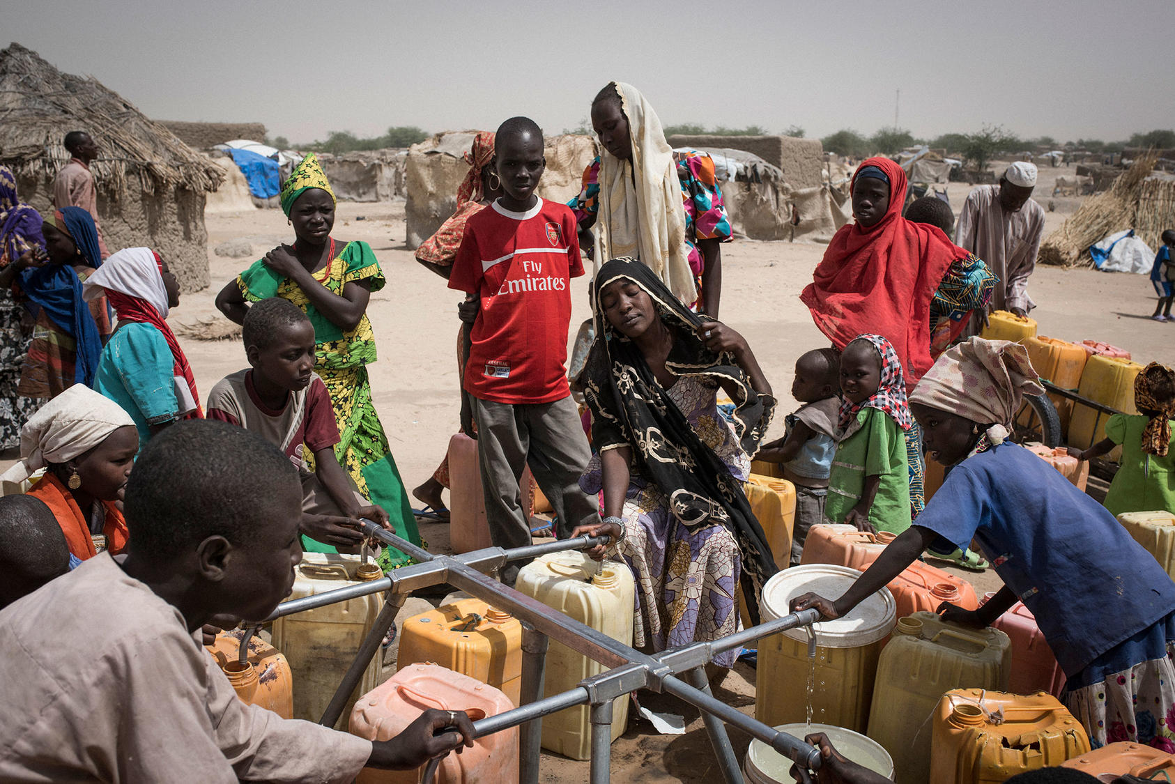 Nigerian refugees collect water from an International Rescue Committee point along National Route 1,