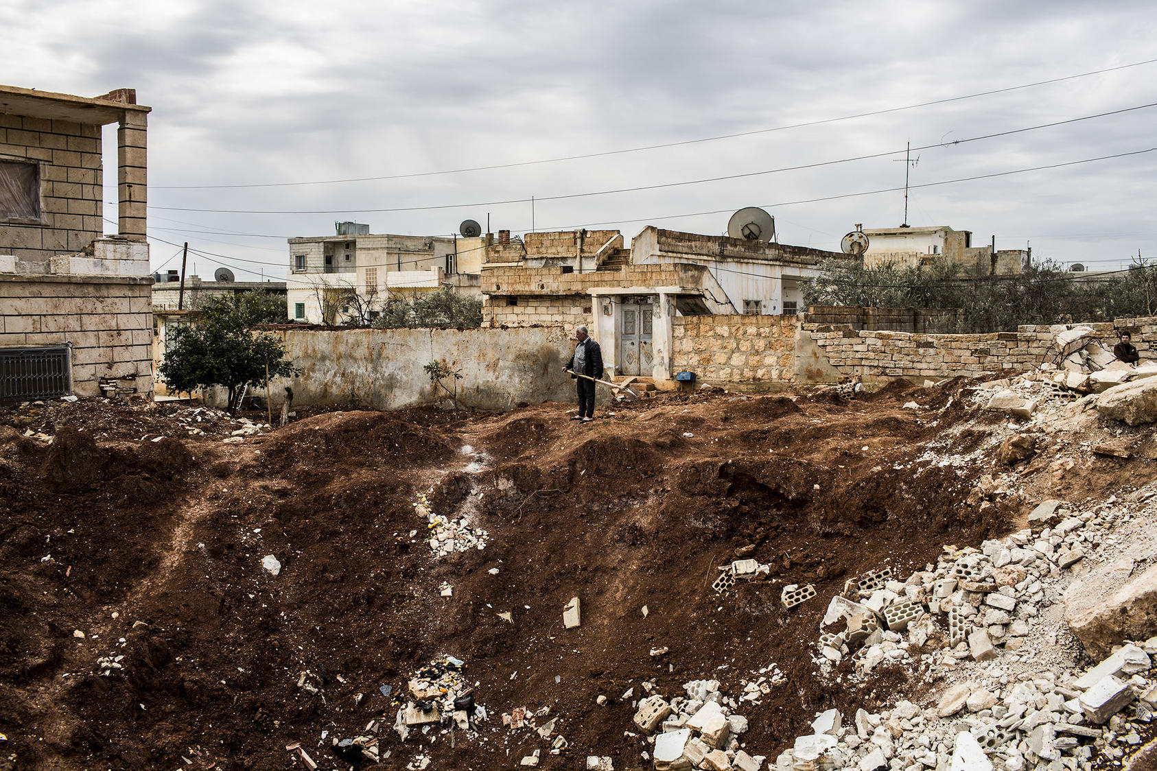 A resident of Syria’s Idlib province surveys a crater from a missile strike in 2013. As the province faces a new offensive, its nascent women’s movement has had to close some of its education centers for women and girls. (Bryan Denton/The New York Times)