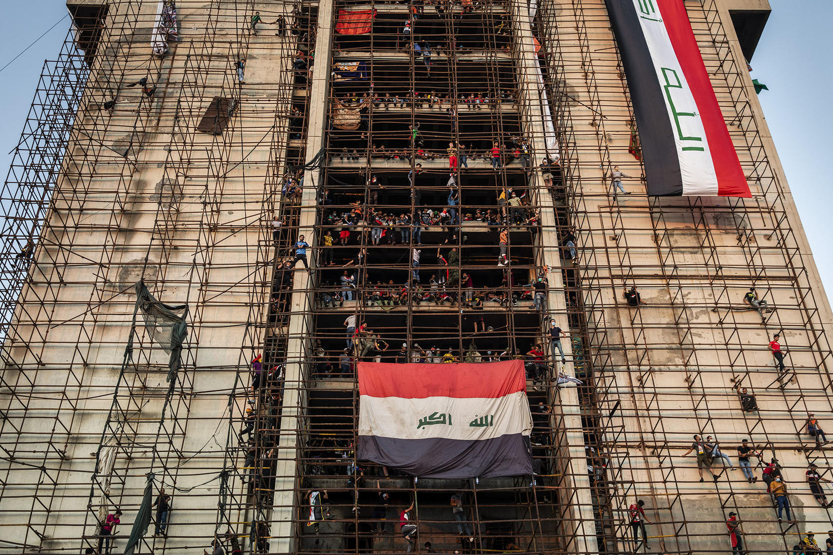 Young men climb scaffolding to reach the upper levels of an unfinished building overlooking mass protests in Tahrir Square in Baghdad, Nov. 1, 2019. (Ivor Prickett/The New York Times)