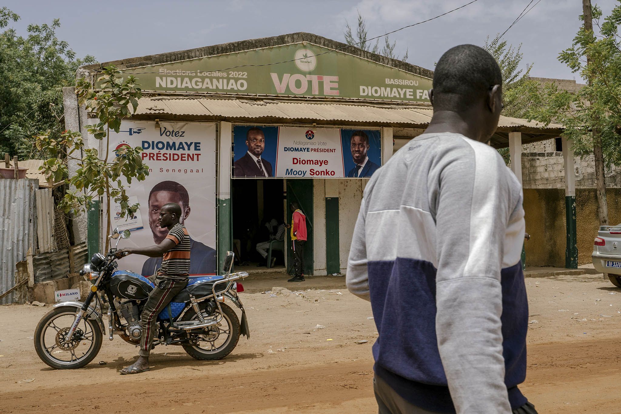 Men pass a campaign office of Senegal’s newly elected president, Bassirou Diomaye Faye, in his family village. Faye’s election ends a Senegalese political crisis and can let the country consolidate its democracy. (Carmen Abd Ali/The New York Times)