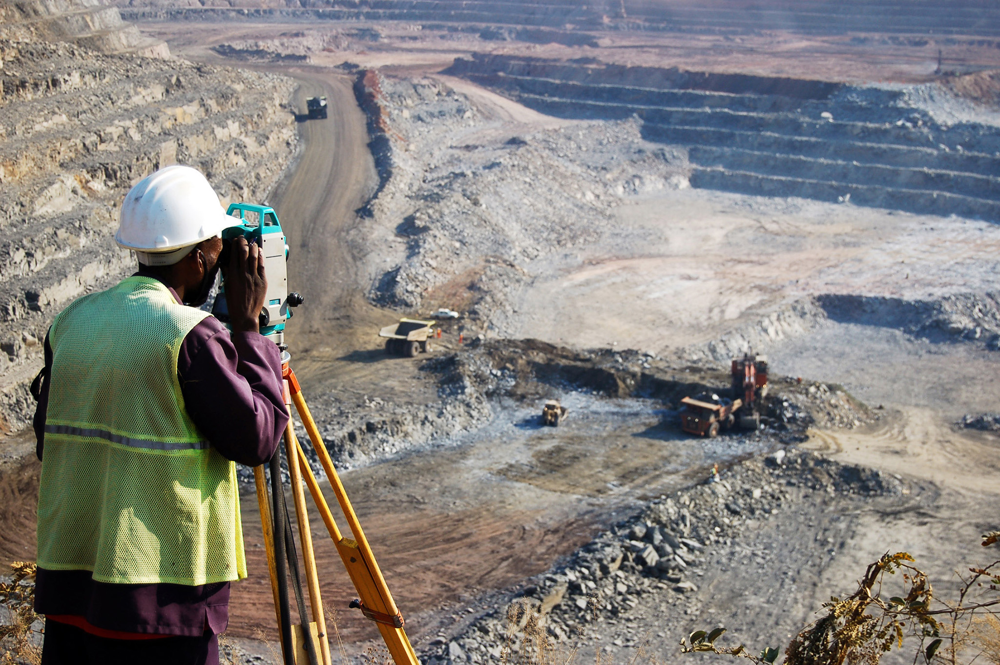 A locally employed surveyor at an open-pit copper mine in Zambia peers through a theodolite to record the daily changes in the mine and to help guide mining activities. (Photo by mabus13/iStock)