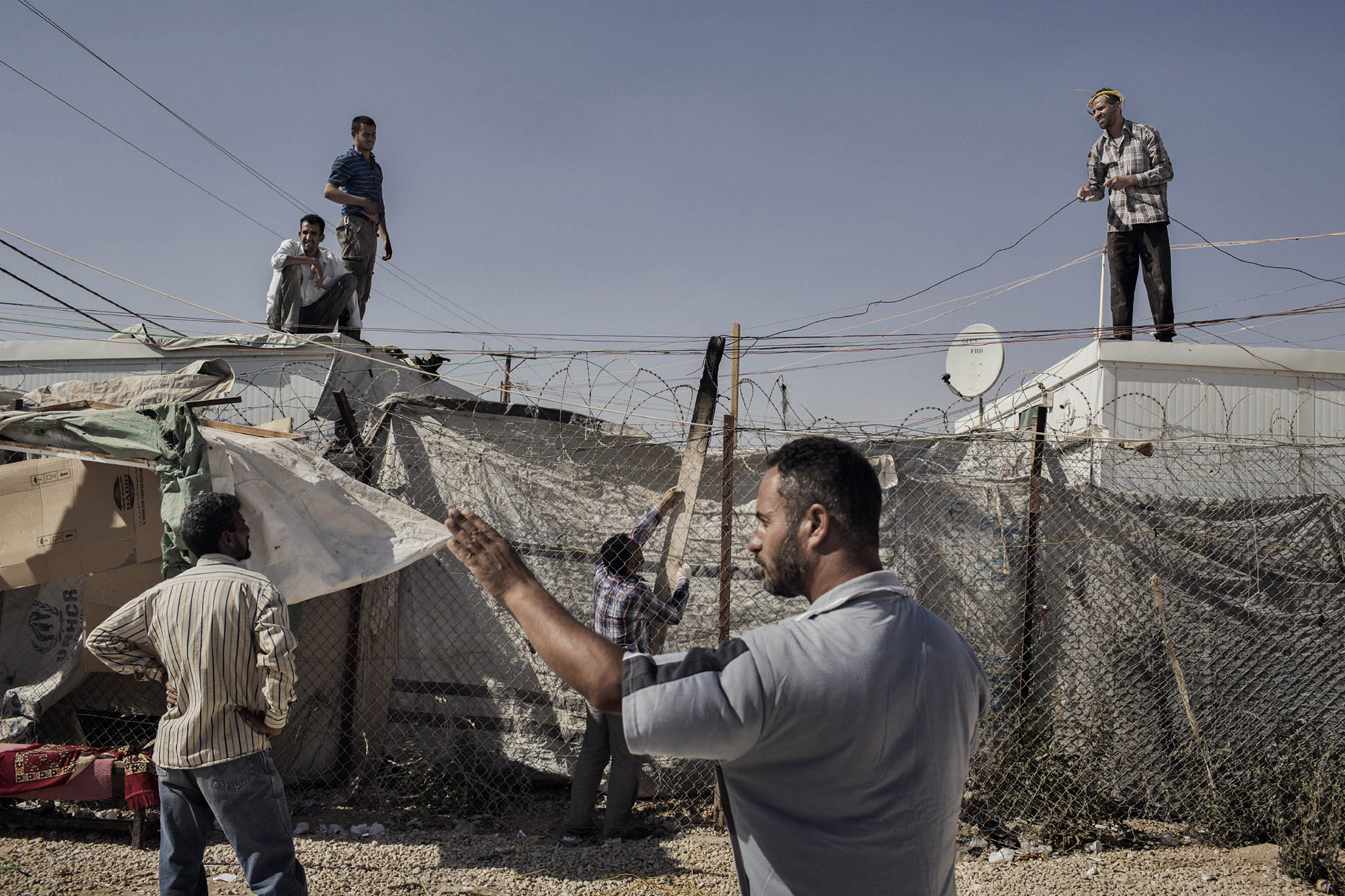 Syrian men attach wires to an electrical circuit in order to power their homes in the Zaatari refugee camp in Jordan, June 23, 2014. (Adam Ferguson/The New York Times)