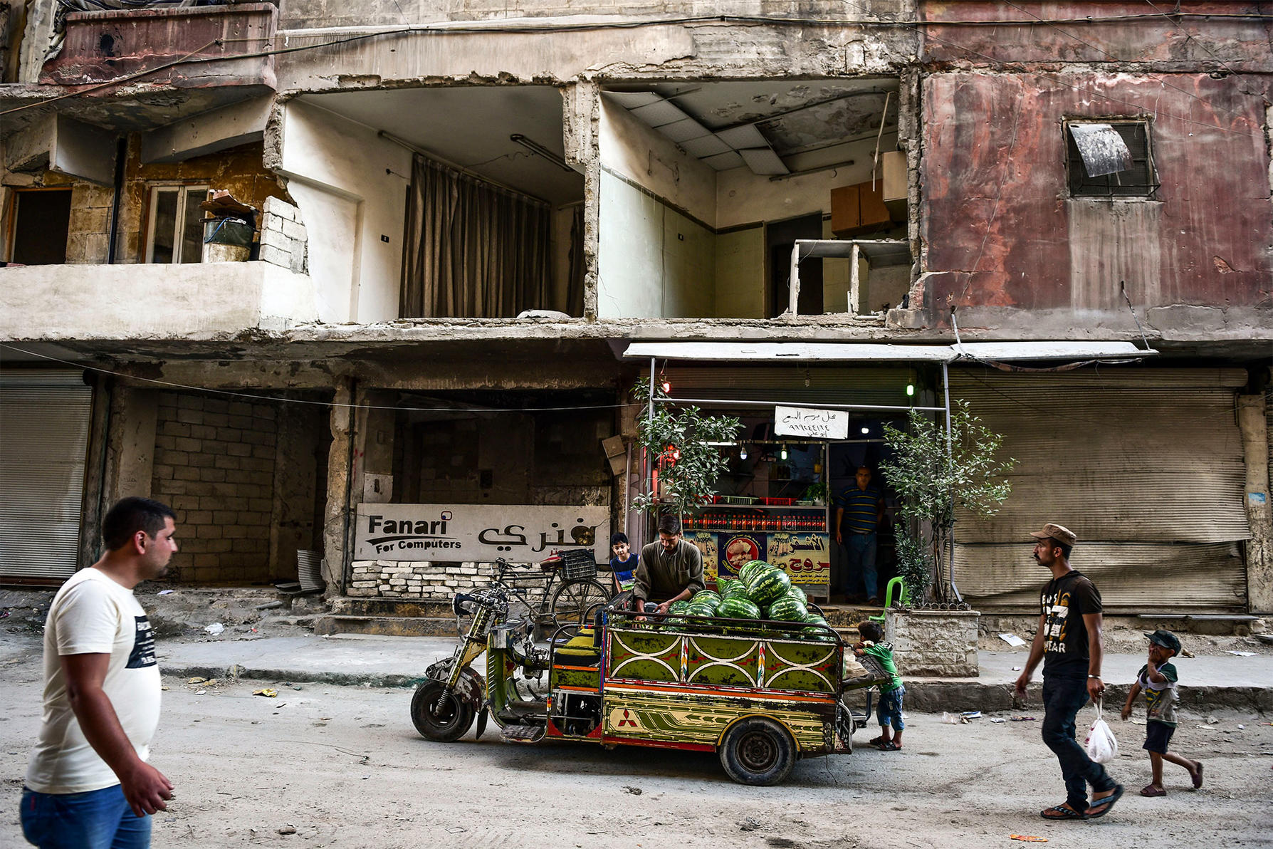A man selling watermelon in front of buildings destroyed by government forces in eastern Aleppo, Syria, June 23, 2019. (Meridith Kohut/The New York Times)