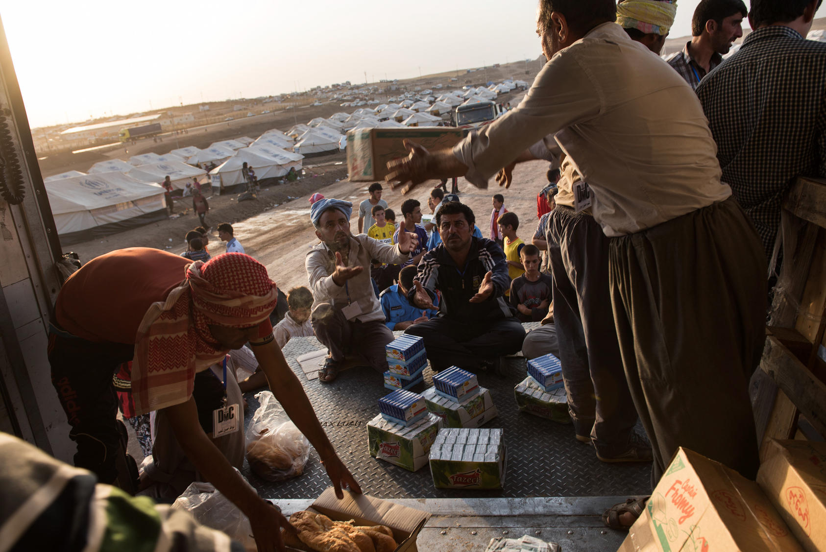 Men working on behalf of the Kurdish government hand out food and juice to Iraqi Yazidi families at the Bajid Kandal refugee camp in Dohuk Province, northern Iraq, Aug. 17, 2014. The spread of the Islamic State group has displaced many Christians and Yazidis.