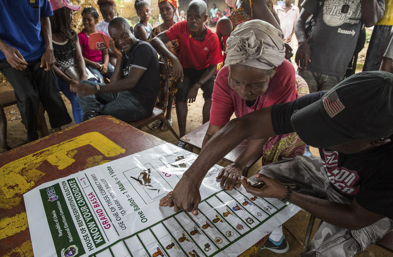 A member of Joseph Duo's campaign team shows a woman where the candidate's name will appear on the ballot in District One of Grand Bassa County, Liberia, Sept. 28, 2017. Photo courtesy of Carielle Doe/The New York Times.