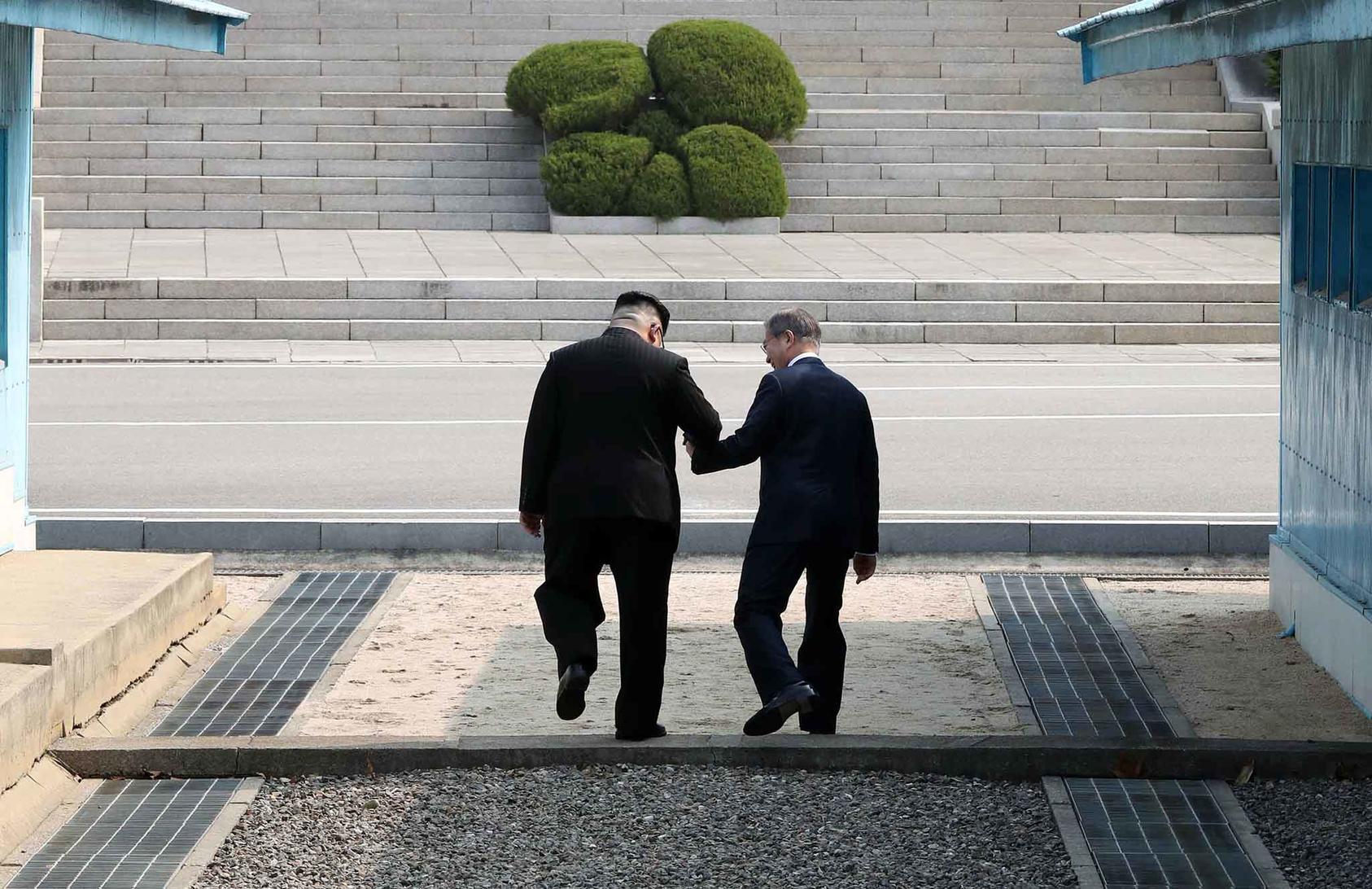 North Korean leader Kim Jong-un, left, holds South Korean President Moon Jae-in's hand as they step over the border demarcation line onto North Korean territory, in the border village of Panmunjom.  (Korea Summit Press Pool via The New York Times)