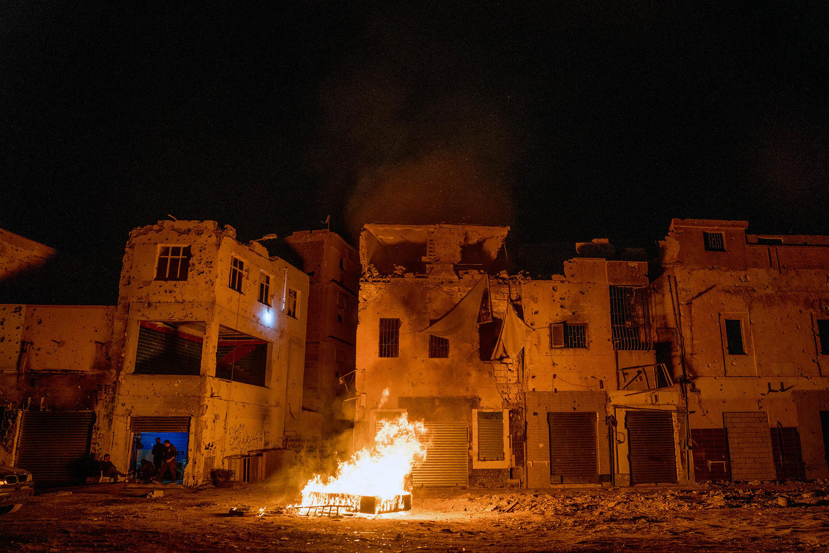 In the devastated downtown, of Benghazi, Libya, ex-fighters warm themselves over a bonfire made from broken furniture in March 2018. (Declan Walsh/The New York Times)