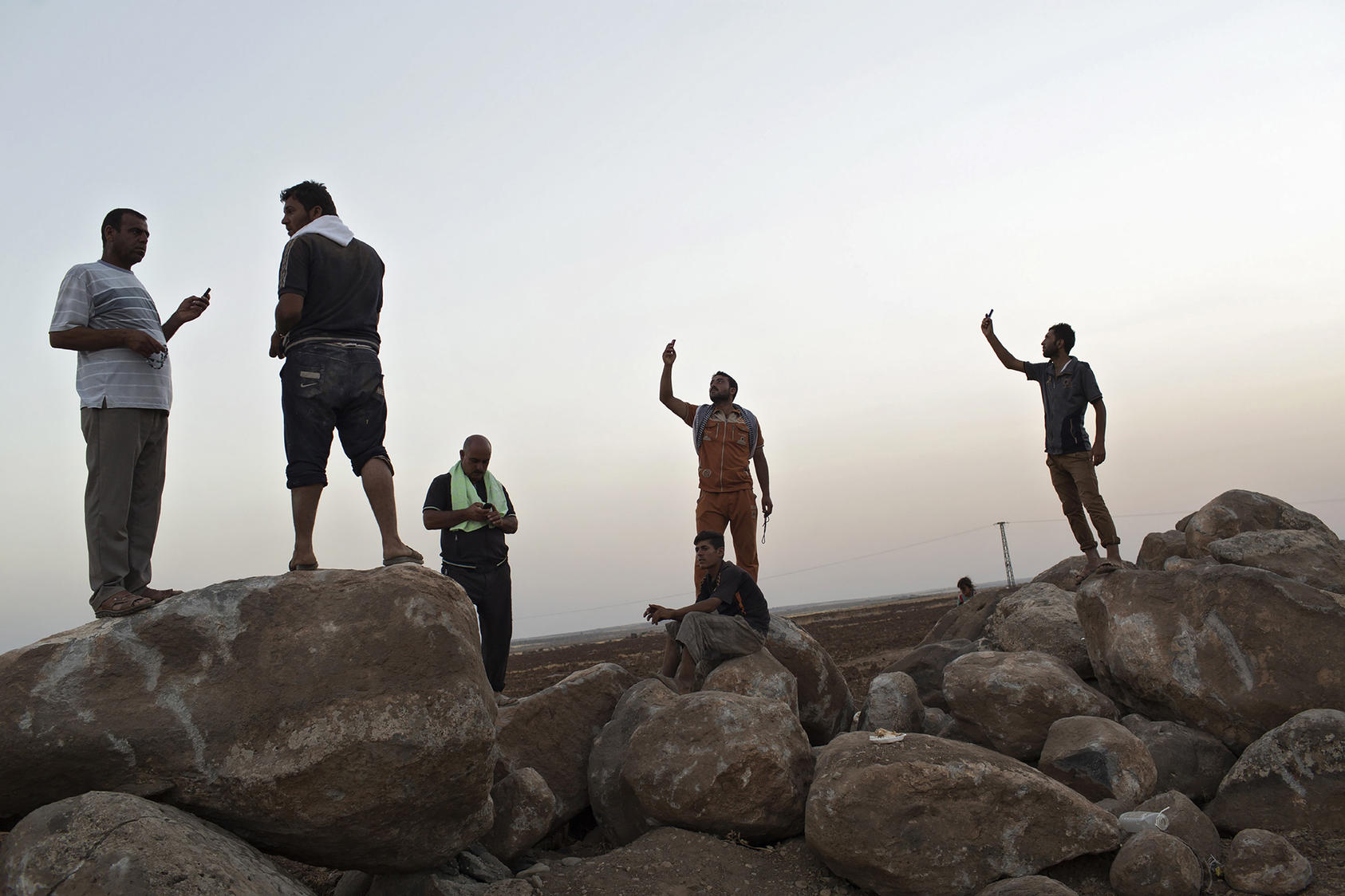 Iraqi Yazidis try to get better cell phone reception from atop boulders at a refugee camp in Derik, Syria, Aug. 10, 2014. (Adam Ferguson/The New York Times)