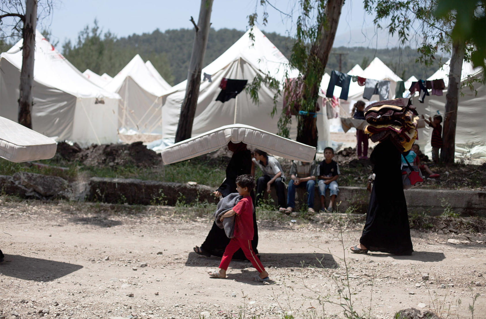 Women carry a mattress and blankets through a Syrian refugee camp in Yayladagi, Turkey on June 10, 2011. (The New York Times)