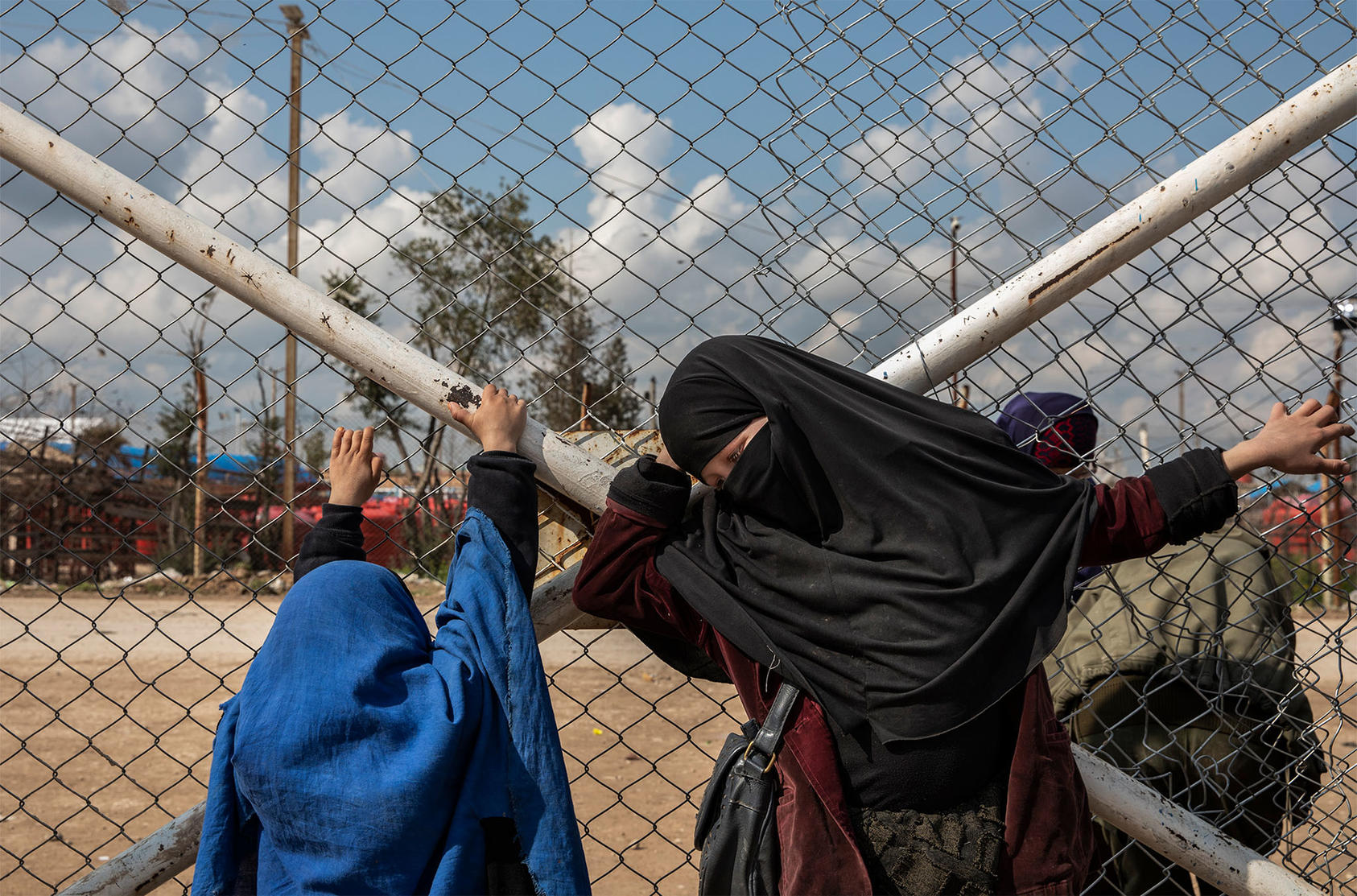 A girl and woman at the fence of the al Hol camp are among thousands who lived under ISIS’ rule. Many are stranded in the camp’s ISIS-influenced environment as governments decline to repatriate them. (Ivor Prickett/The New York Times)