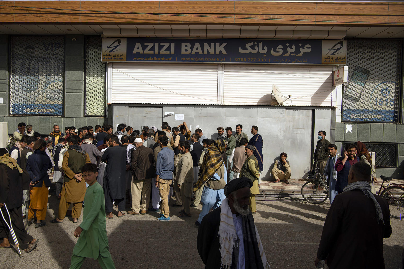Afghans wait to withdraw money from a bank in Mazar-i-Sharif, Afghanistan, on Oct. 9, 2021. (Kiana Hayeri/The New York Times)