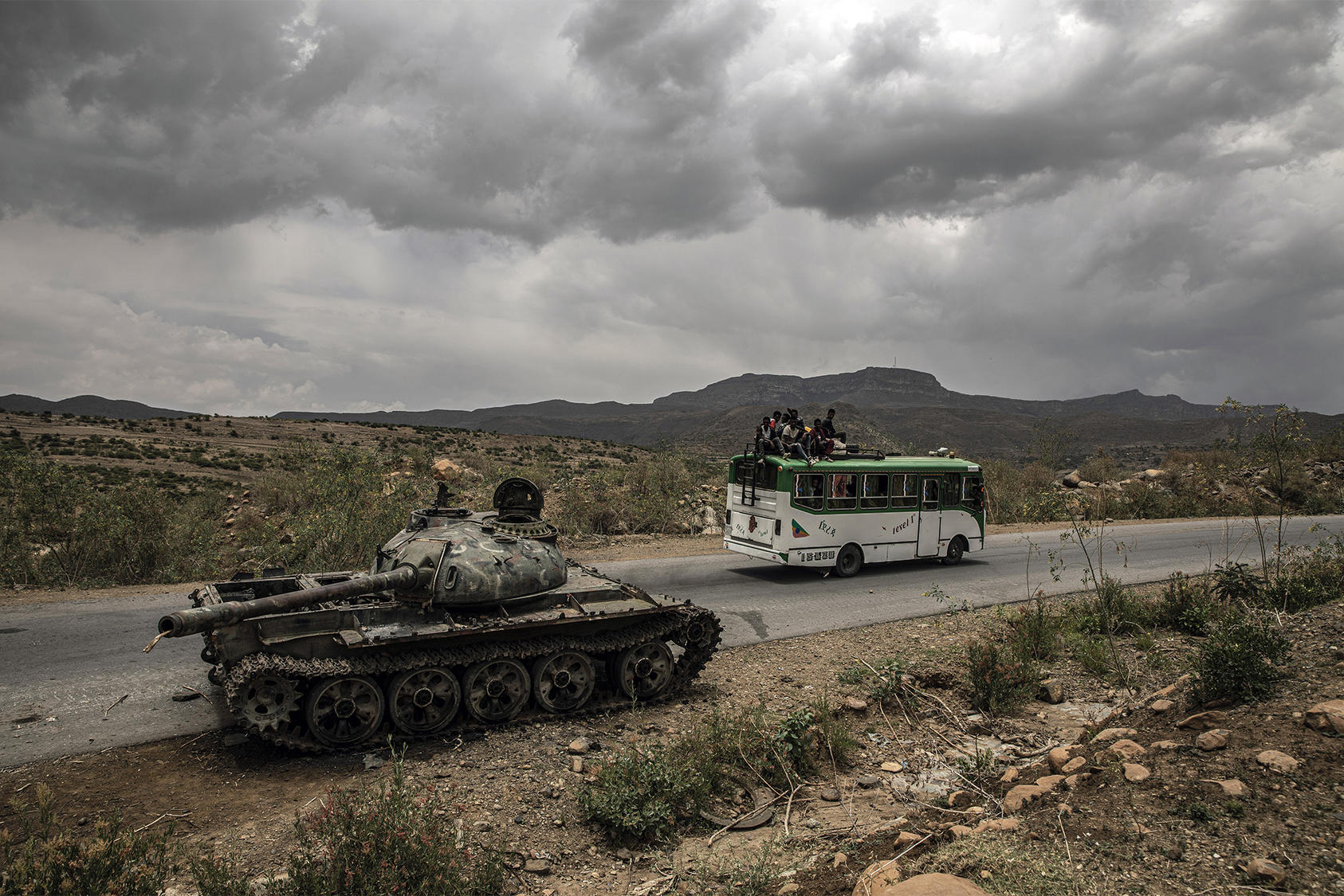 Civilians ride in and on a bus past a damaged tank outside Mekelle in Ethiopia’s Tigray region last year. Implementing a humanitarian truce in the war will require careful steps on the ground to avoid violations. (Finbarr O'Reilly/The New York Times)