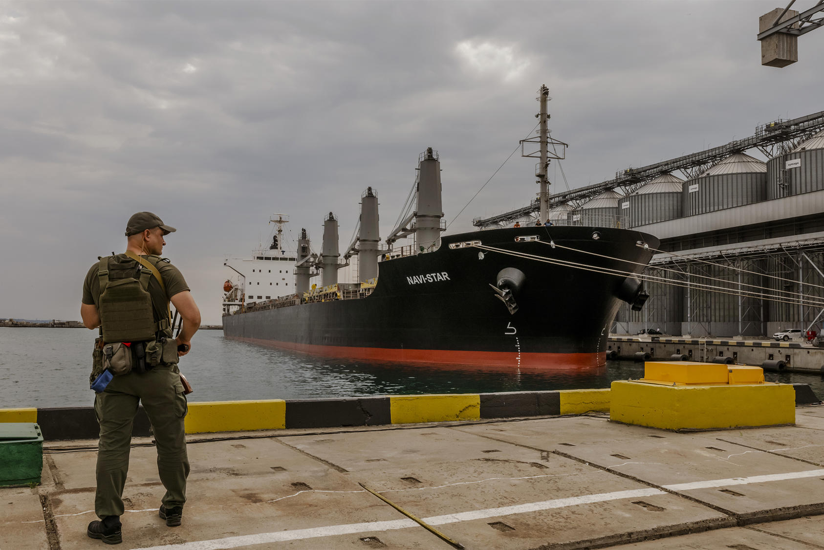 A Ukrainian soldier guards a bulk cargo ship and grain silos in Odesa, Ukraine’s biggest seaport. One ship has left Ukraine in 12 days since Russia signed a deal to permit grain exports and then rocketed Odesa’s port. (Daniel Berehulak/The New York Times)