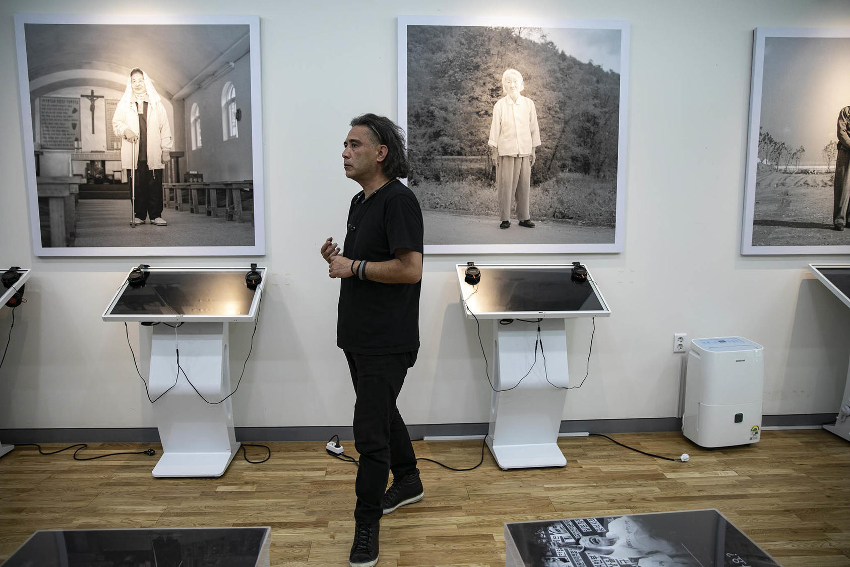 The Japanese photographer Tsukasa Yajima with portraits he took of former Korean “comfort women” at the history museum of the House of Sharing shelter, in Gwangju, South Korea. July 3, 2022. (Woohae Cho/The New York Times)