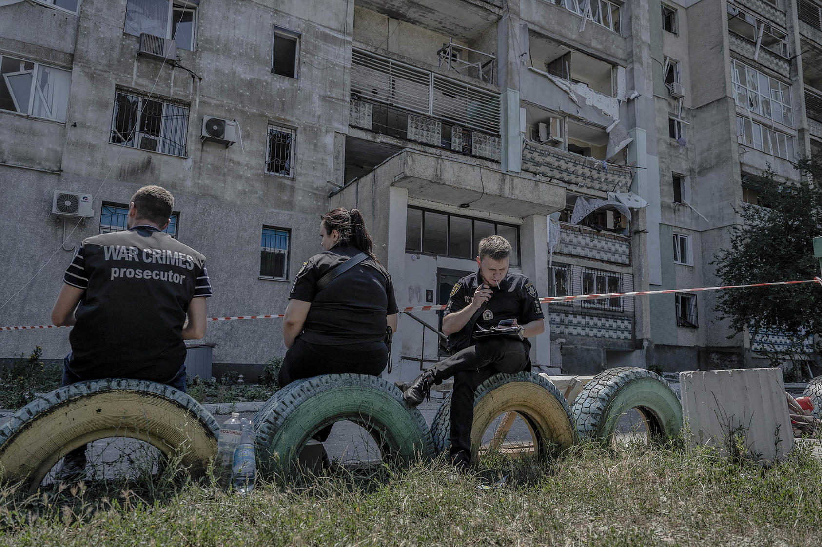 A man with a shirt marked “war crimes prosecutor” with police officers near a residential tower hit by a Russian missile in the Serhiivka village of the Bilhorod-Dnistrovskyi district, Ukraine, July 1, 2022. (Laetitia Vancon/The New York Times)]