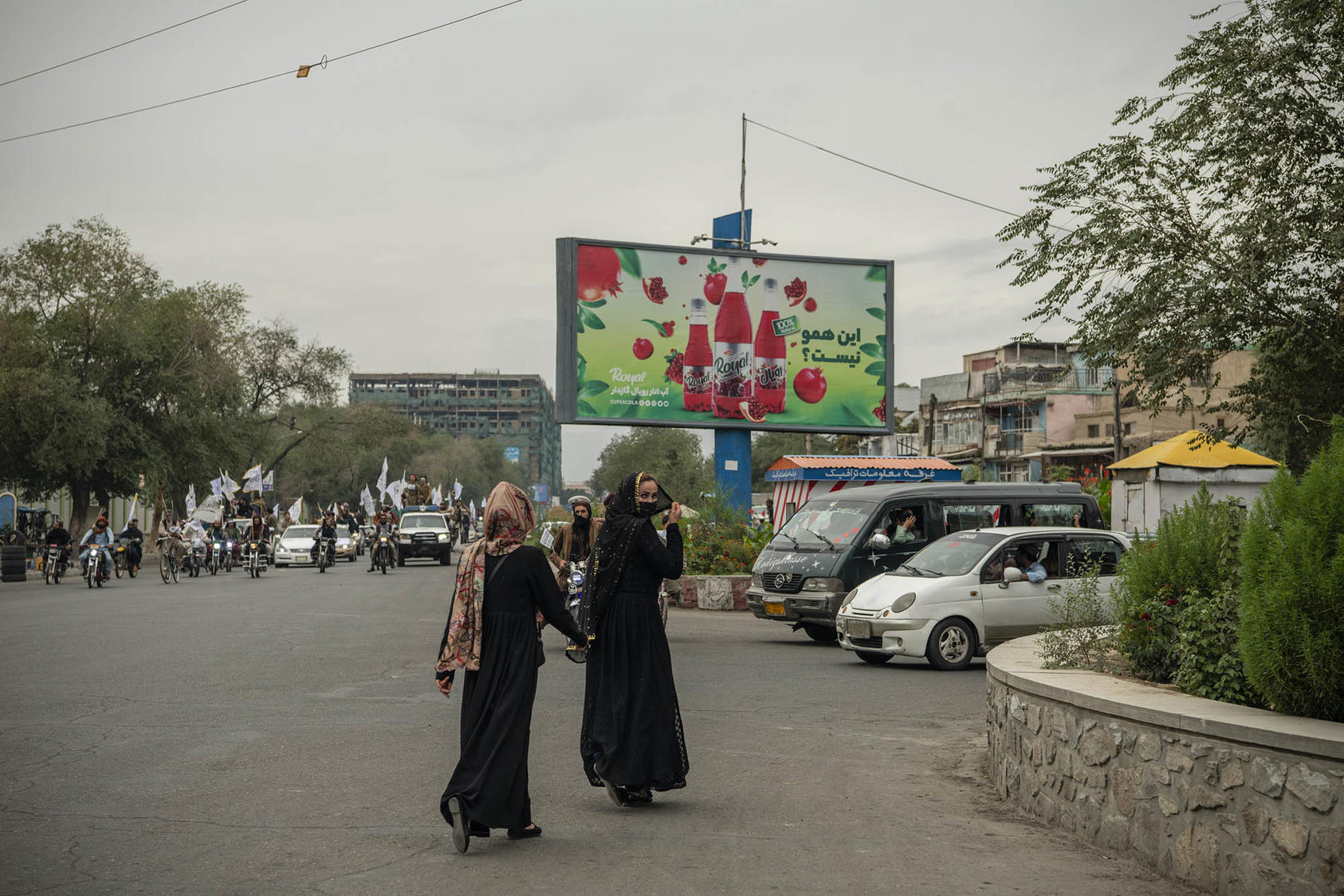 Women cross a street in front of Taliban fighters celebrating the first anniversary of the Taliban takeover of Kabul on Aug. 15, 2022. (Kiana Hayeri/The New York Times)