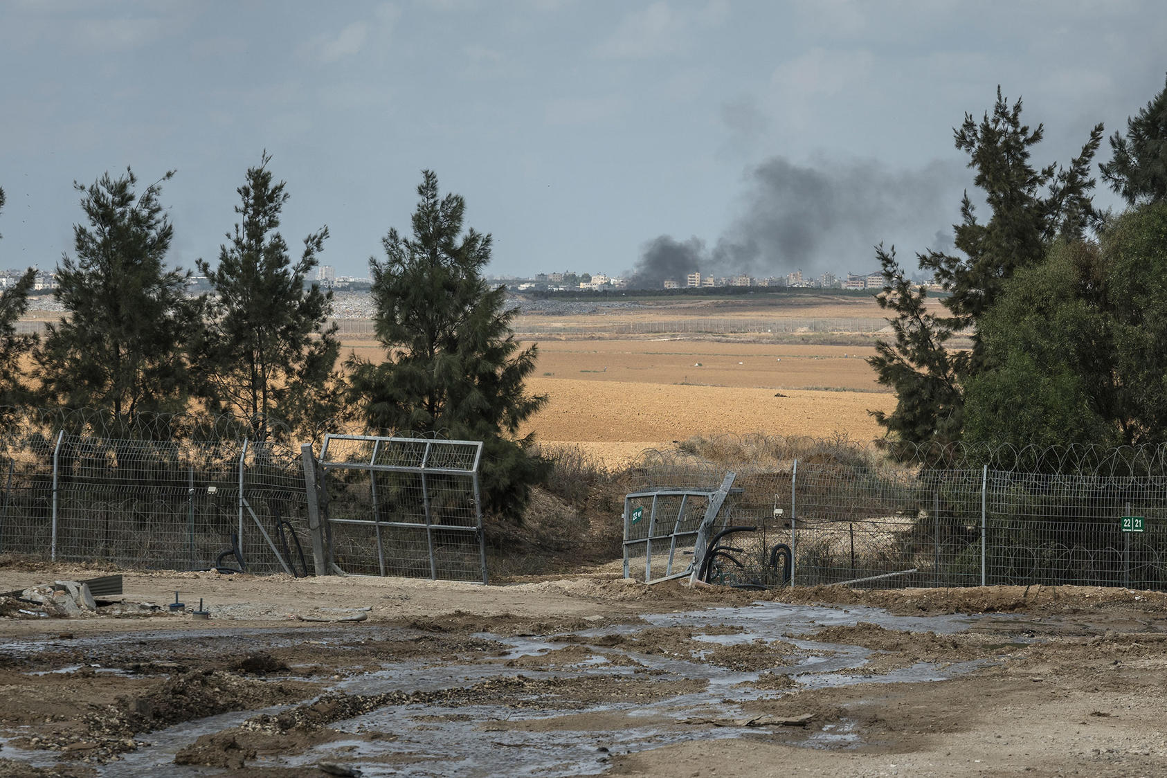 Smoke rises in Gaza City in the distance above the broken security fence at Kfar Azza, a village just across the border from Gaza that was attacked by Palestinian gunmen, in Israel, Tuesday, Oct. 10, 2023. (Sergey Ponomarev/The New York Times)