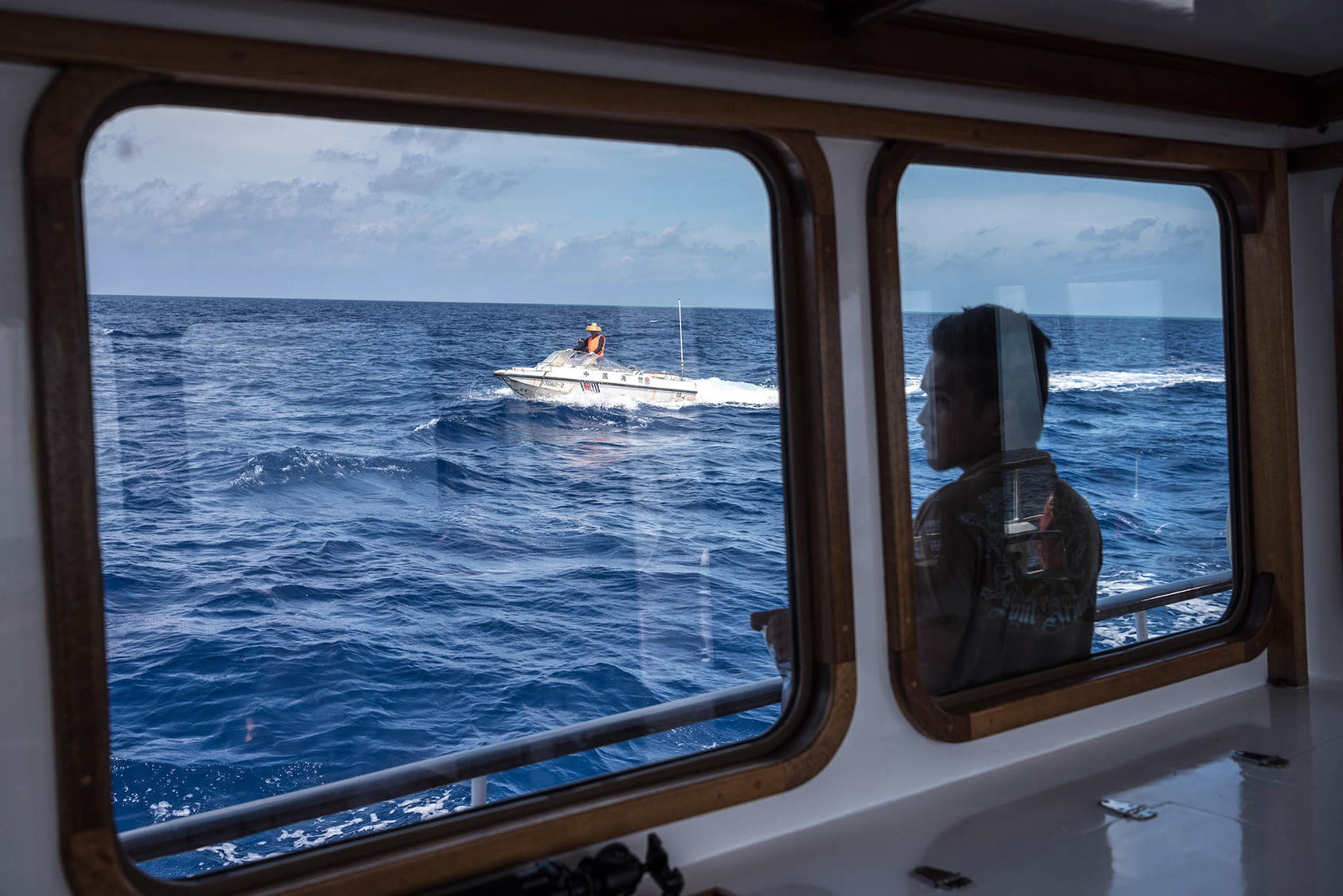A speedboat launched from a Chinese Coast Guard vessel is seen through a window of the Motoryacht Isla, based in the Philippines, demanding it leave the Scarborough Shoal in the South China Sea, June 18, 2016. (Sergey Ponomarev/The New York Times)