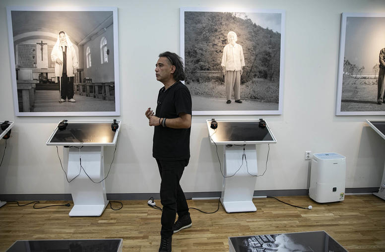The Japanese photographer Tsukasa Yajima with portraits he took of former Korean “comfort women” at the history museum of the House of Sharing shelter, in Gwangju, South Korea. July 3, 2022. (Woohae Cho/The New York Times)