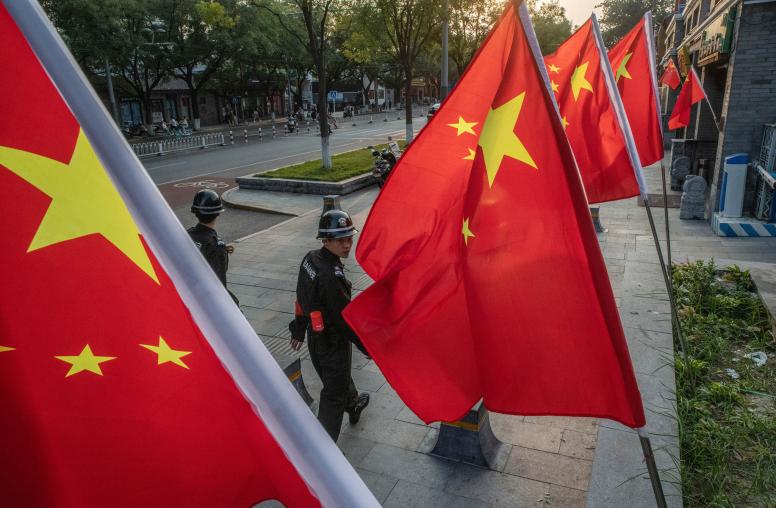 Security guards walking past Chinese flags decorating a street in Beijing. October 1, 2019. (Gilles Sabrie/The New York Times)